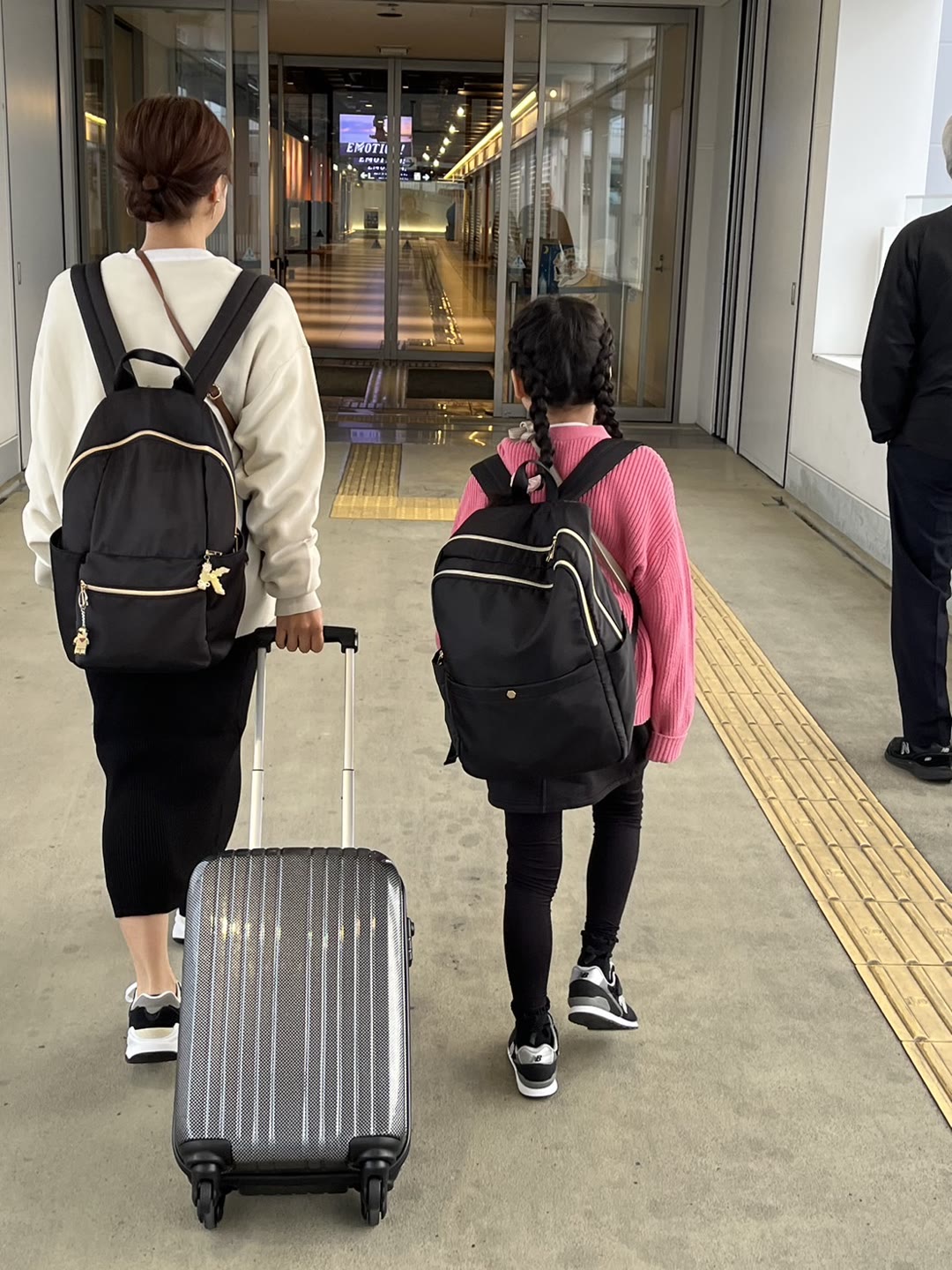 朝一のLCCで九州へ。空港の連絡通路をスーツケースを引いて歩く親子の後ろ姿